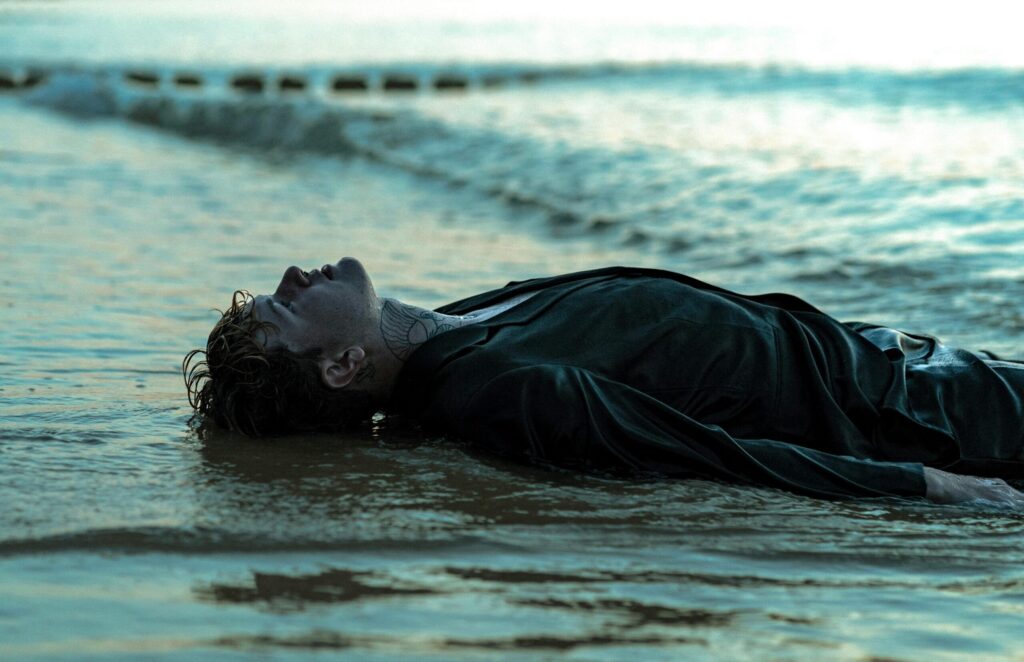 A man in wet clothes lies by the sea, capturing a dramatic and emotional moment.